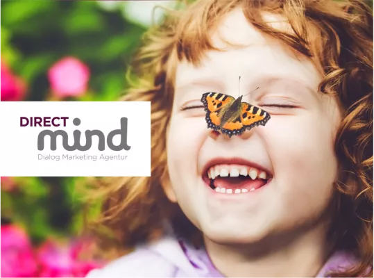The purple-grey logo of “DIRECT mind” “Dialog Marketing Agency”. The logo stands out on a white background against the background image of a cheerful child with a butterfly on its nose. 