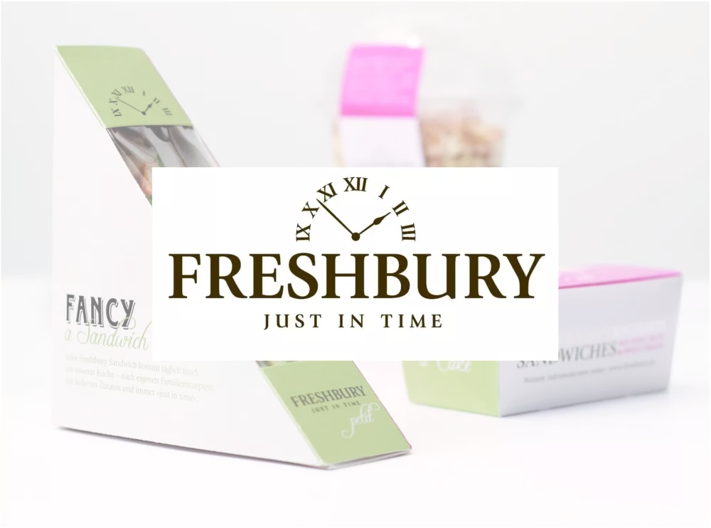 The Freshbury logo (a section of a clock with Roman numerals, below which is FRESHBURY, below which is JUST IN TIME), behind which is a selection of packaged sandwiches. 