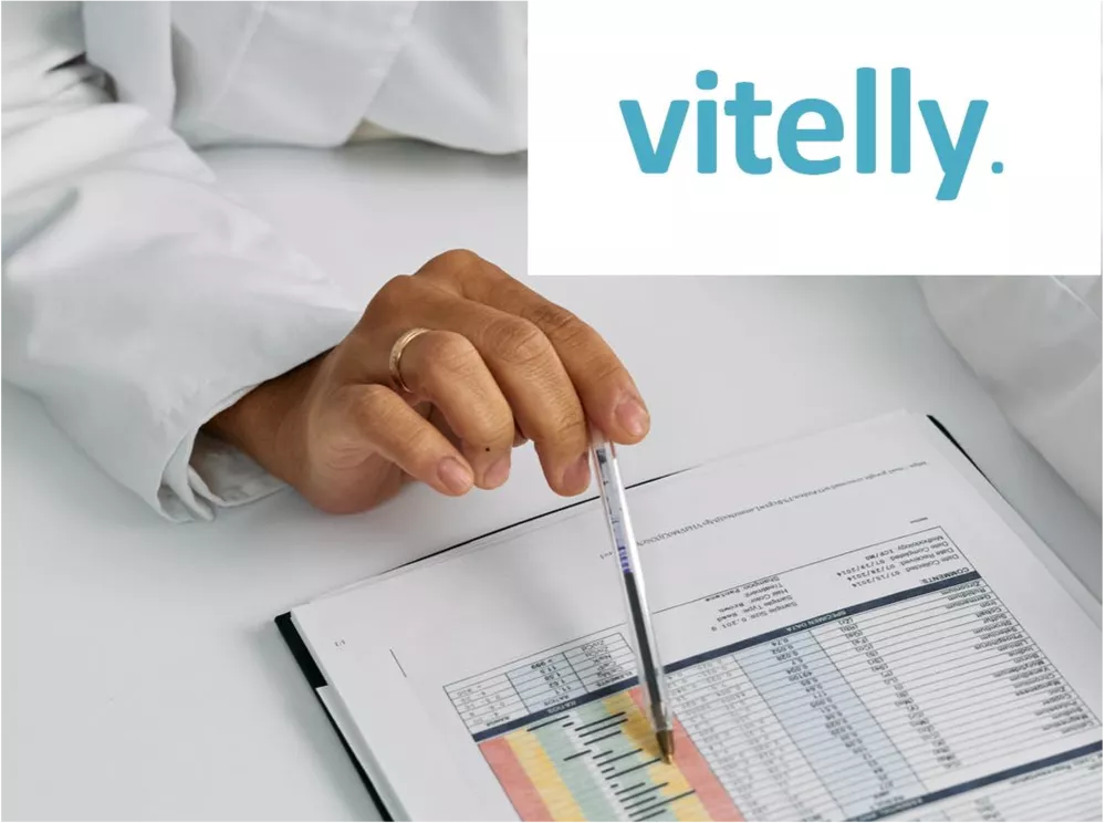 A hand with a pen and white coat points to a paper with parameters. The vitelly logo is at the top right of the picture. 